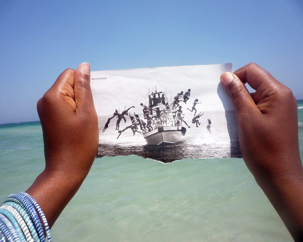 A POV photo of two hands holding a torn picture of people jumping off of a boat