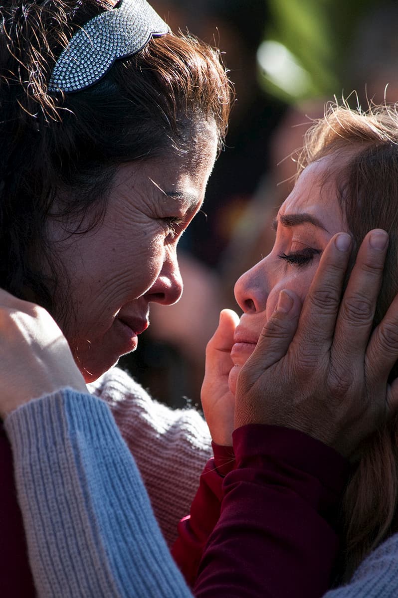 Photograph depicting two women embracing. The older woman on the left holds the younger woman's face in her hands