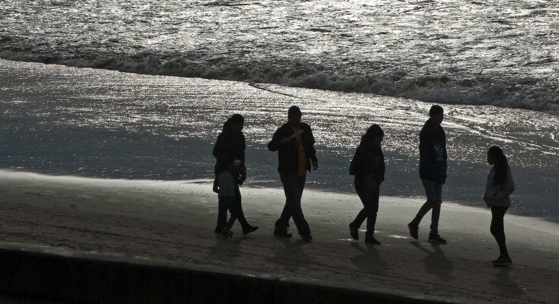 Photograph by Tish Lampert showing 5 silhouetted figures walking along the beach at sunset